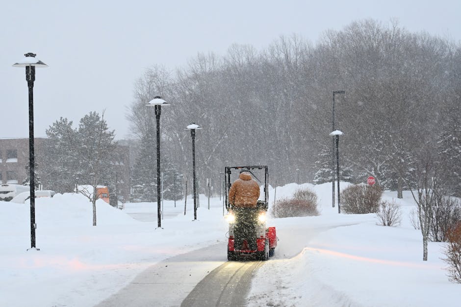A worker clearing a snowy park path with a walk-behind snow blower